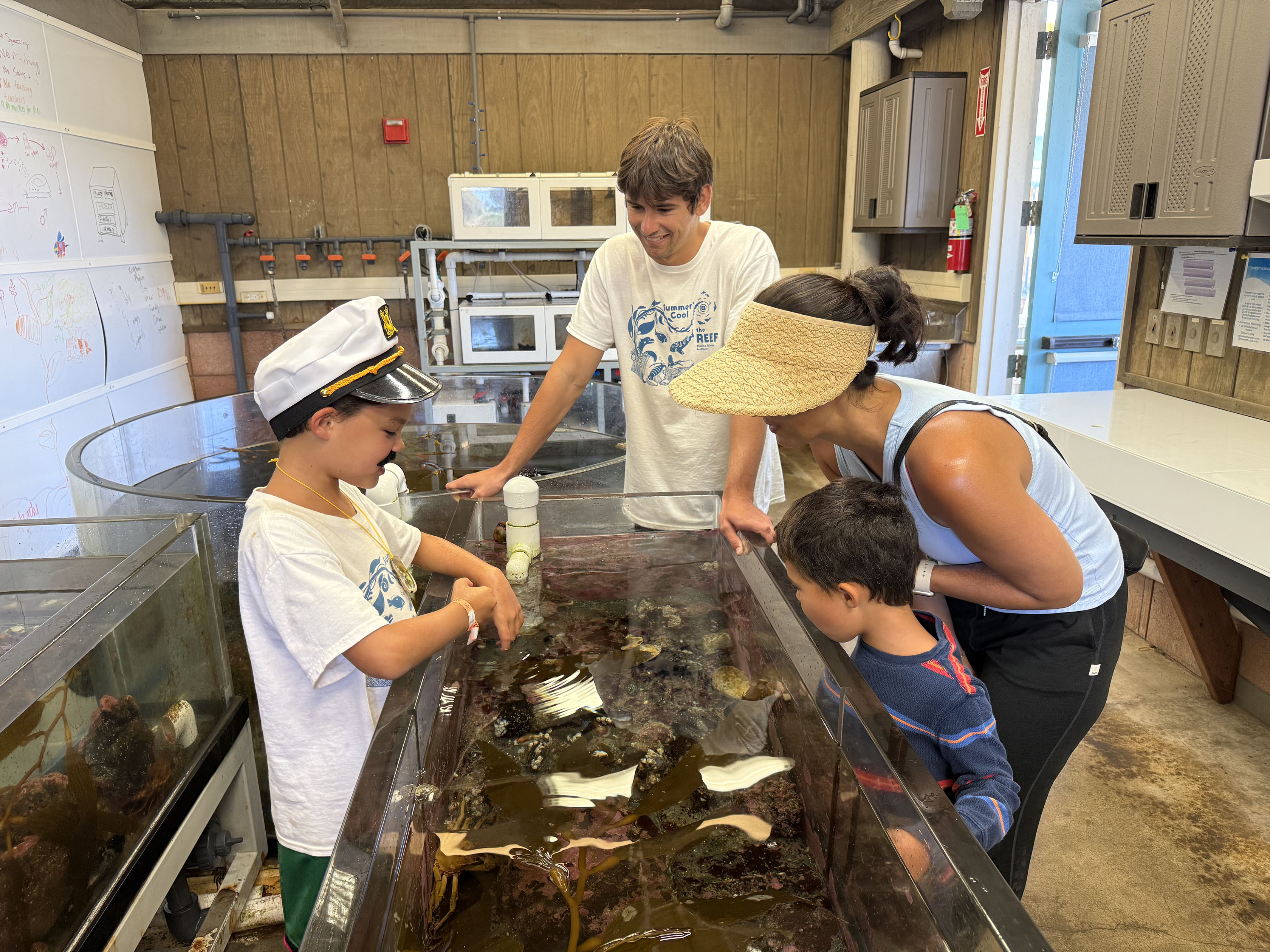 camper showing a mom the critters in touch tank supervised by undergrad student